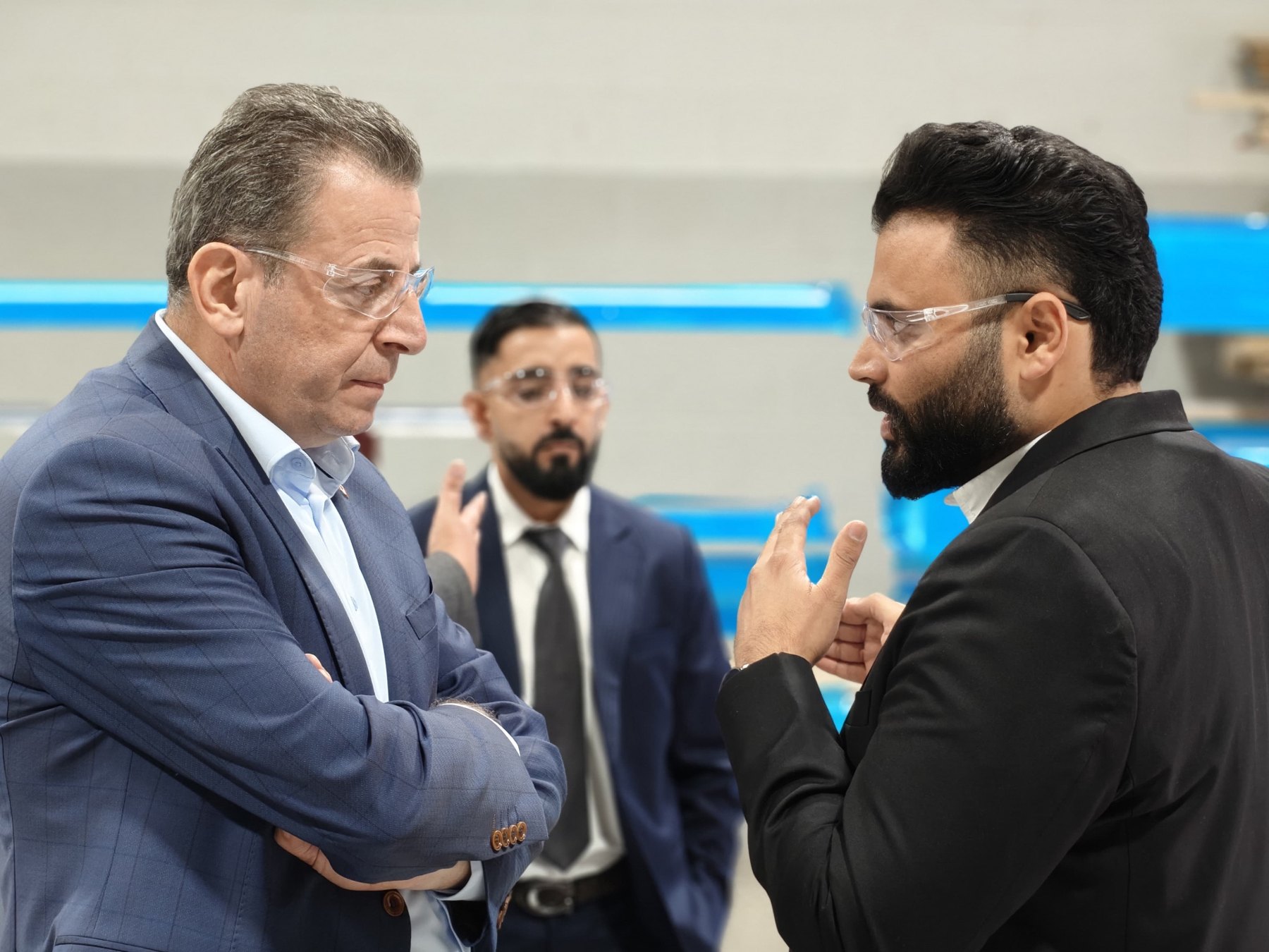 A Member of Parliament listens as a company representative explains operations, both wearing safety glasses.
