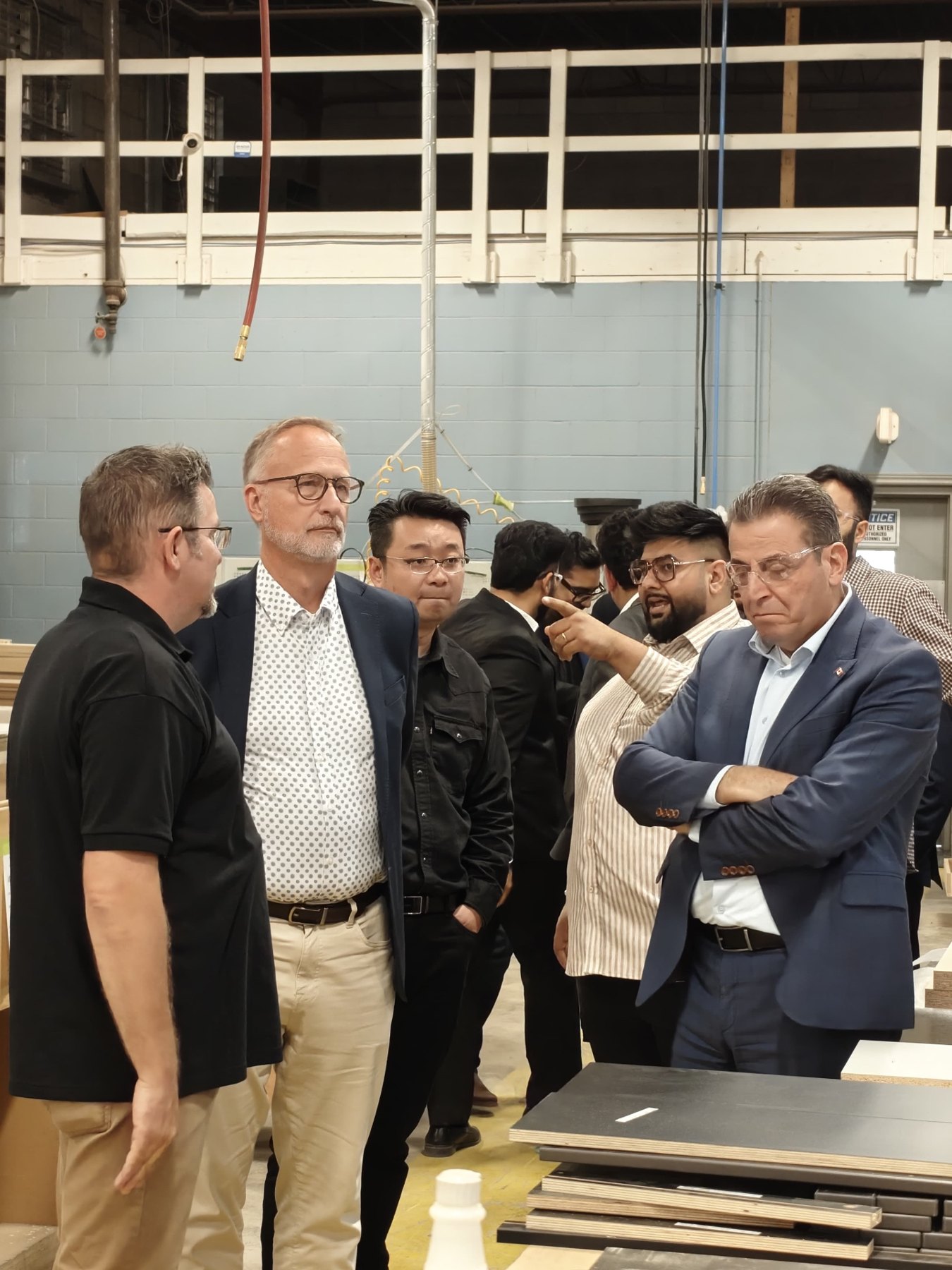 Members of Parliament and guests stand with Sandha staff beside stacked laminated panels on the production floor.