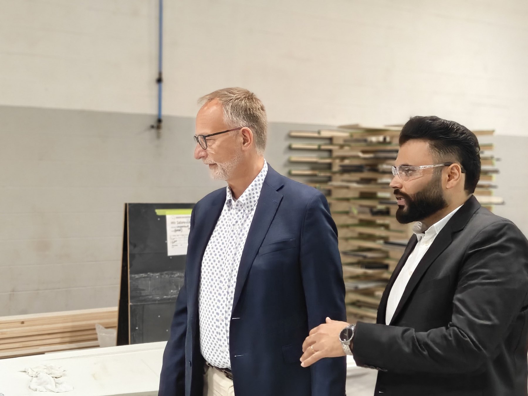 Sandha staff and the visiting delegation in conversation in the production area, with a finishing booth in the background.